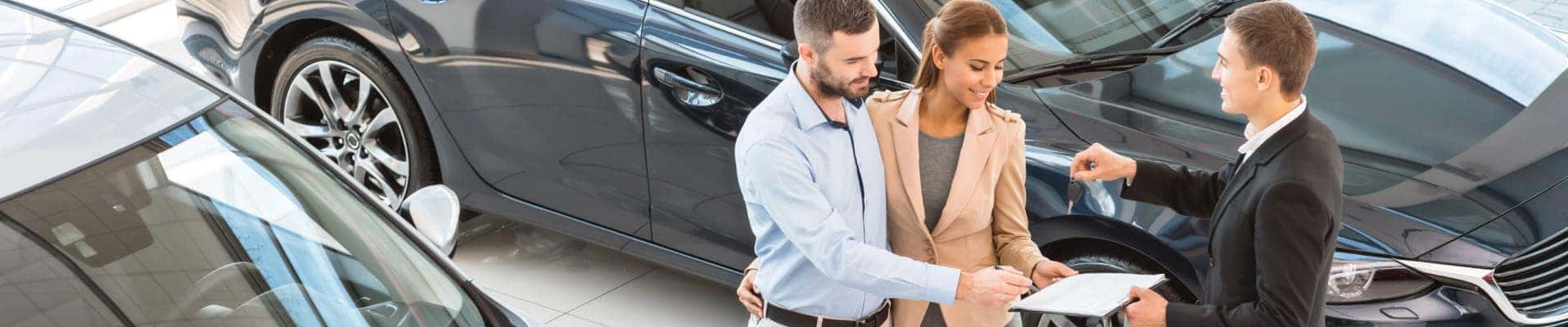 Couple reviewing paperwork with a salesperson while shopping for a vehicle.
