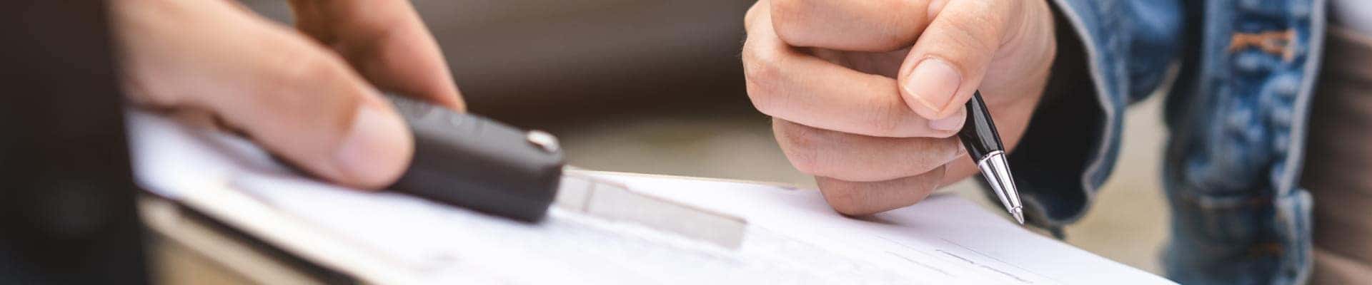 Customer holding a car key and pen while completing vehicle paperwork.
