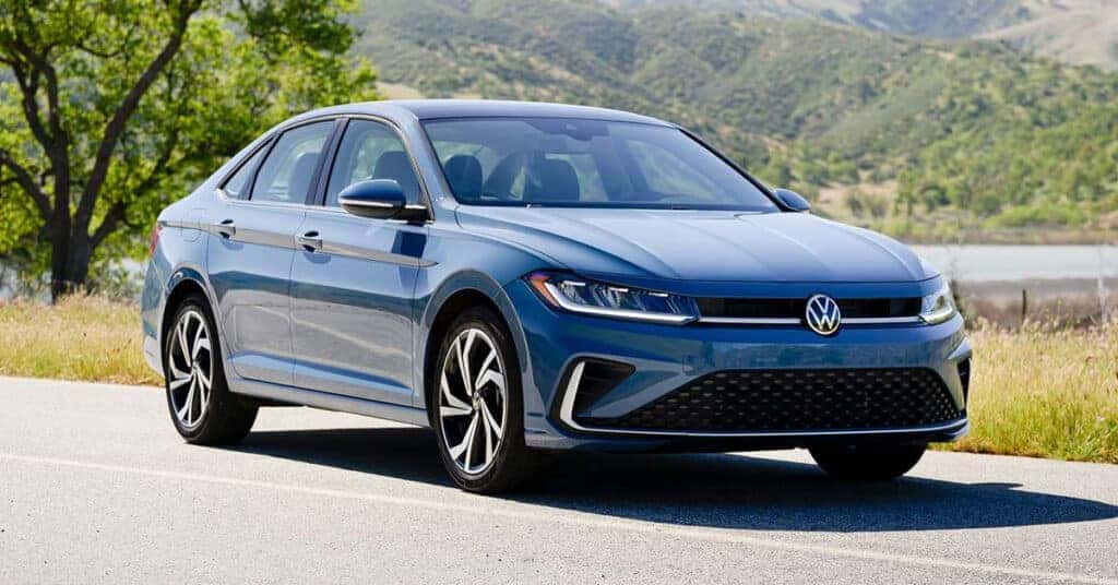 2026 Volkswagen Jetta sedan parked on a scenic road with trees and mountains.