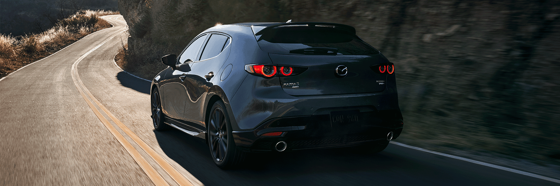 Lancaster Mazda is a Mazda Dealership near Reading, PA | Rear View of Black 2021 Mazda 3 Hatchback Driving up Winding Road in Mountains
