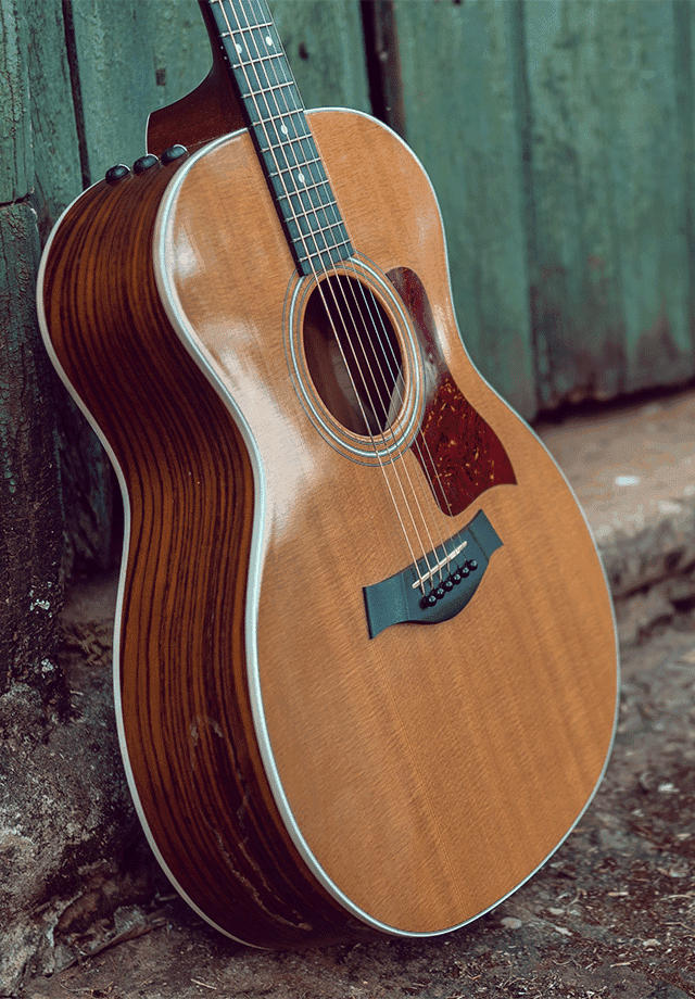 Lancaster Mazda is a Mazda Dealership near Reading, PA | Guitar Proped Up Against Cement Curb and Wood Wall Facing Right