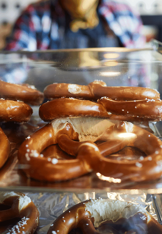 Lancaster Mazda is a Mazda Dealership near Reading, PA | Pretzels Sitting on Tray in Display Case at Bakery Slightly Stacked on One Another In Foreground while Baker is Blured in Background Behind Counter