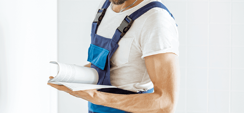 Extend the Life of Your Vehicle at Lancaster Mazda in East Petersburg, PA | Mechanic in blue and white uniform is reading car owners manual  