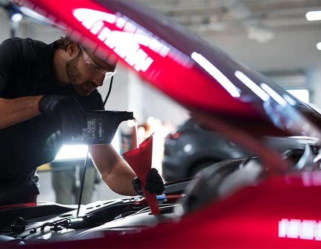 3 Main Benefits of Using OEM parts for your vehicle at Lancaster Mazda in East Petersburg, PA | Mazda mechanic pouring in OEM Mazda engine oil