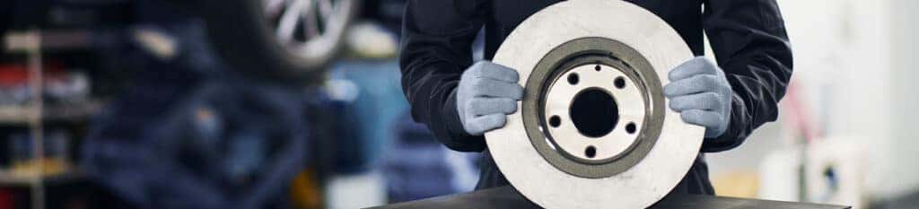 Brake replacement and Safety at Lancaster Mazda | Mechanic holding a brake pad while wearing protective gloves