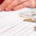 close up of hand signing paperwork next to car keys