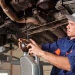 Male mechanic draining the oil from a vehicle during an oil change
