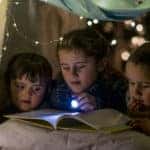 children reading book in pillow fort