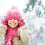 Happy child wearing a tan coat, pink hat, and pink scarf playing on a winter walk in nature