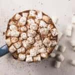 Hot chocolate full of marshmallows in a blue mug. Cocoa powder is sprinkled over the top of the marshmallows.