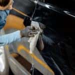 A car detailer carefully washing the exterior of a black car.
