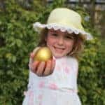 Girl in easter bonnet and dress after an egg hunt. She is holding a golden easter egg.