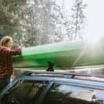 woman loads kayak onto roof of vehicle