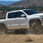 White Nissan Frontier towing equipment on a dirt road