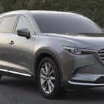 Silver Mazda CX-9 parked in front of a concrete wall with trees behind it
