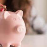 Manicured hand putting a coin into a piggy bank