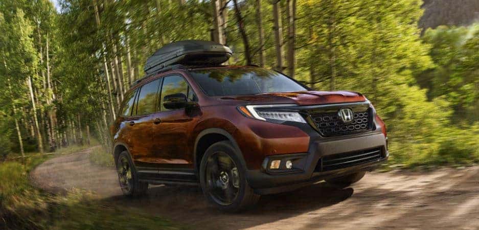 maroon 2021 Honda Passport SUV driving quickly around a bend in a dirt road near trees