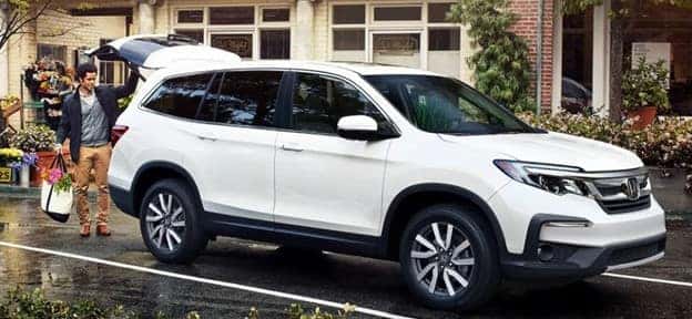 man putting a canvas tote of flowers into the back of a white 2021 Honda Pilot parked near a florist shop
