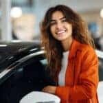 Woman examining a car in a pre-owned vehicle dealership showroom, reflecting the diverse selection and quality assurance.