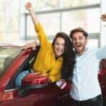 Excited young couple exploring options at a car dealership, embodying the joy of finding the perfect used car, as advised in our comprehensive buying guide.