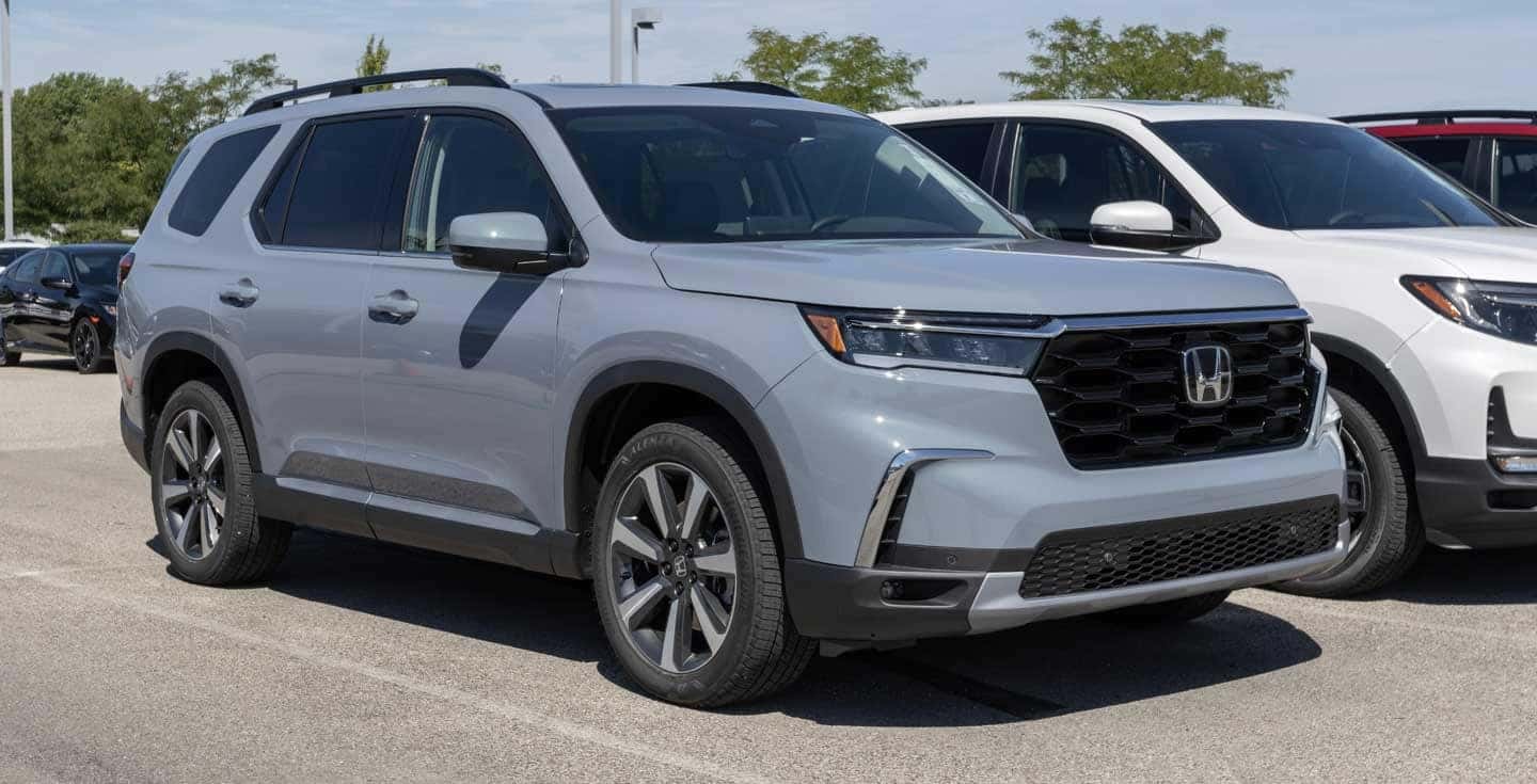 A shiny new Honda Pilot SUV parked prominently on the showroom floor of a dealership, with promotional banners in the background and a salesperson nearby ready to assist potential buyers.
