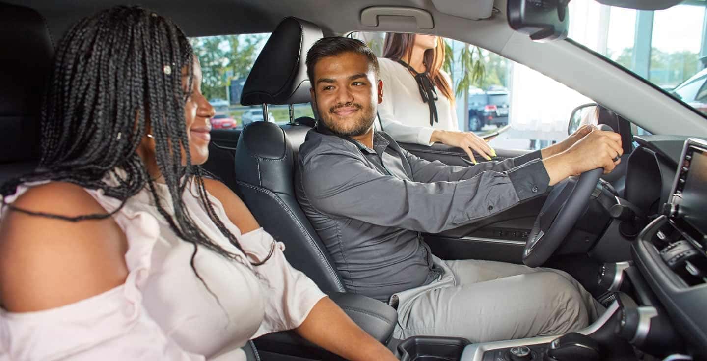 A young emotional married couple discussing with a car sales agent about car finance options near Philadelphia, PA.