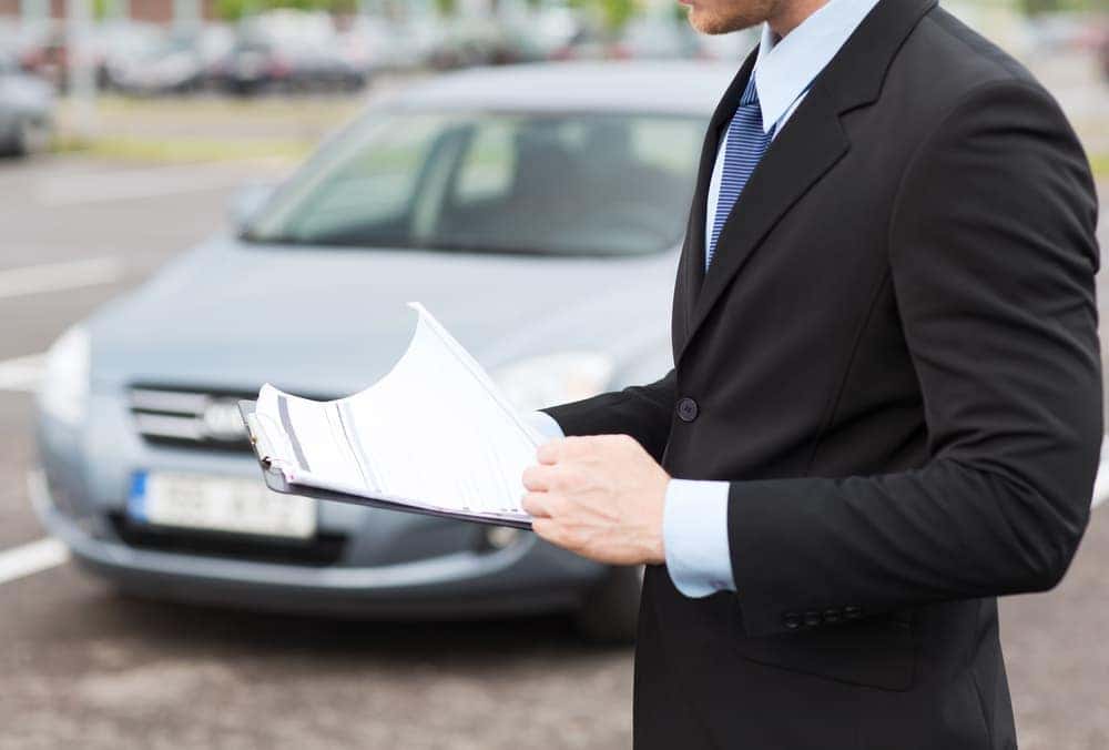 Man with paperwork by a car