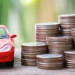 Silver coin of pile with red car model in concept savings to buy a new car or value of car and journey insurance.